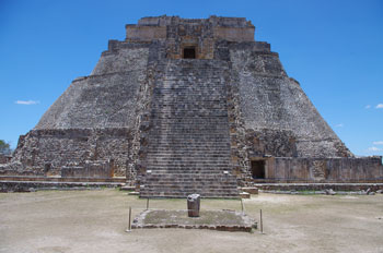 Maya pyramid illuminated from straight above by the Sun with a small taperd stone marker at the foot of the staircase casting a small shadow.