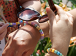 hands holding sunglasses and wearing colorful beads